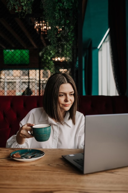 Eine kluge Geschäftsfrau sitzt an einem Tisch in einem Café mit einer Tasse Kaffee und arbeitet an einem Laptop