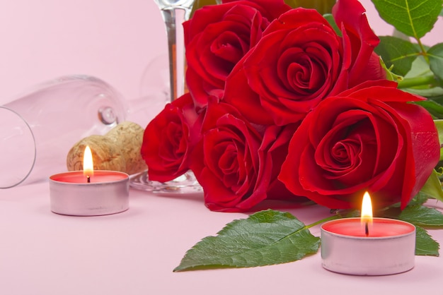 Eine Komposition aus einem wunderschönen Strauß Rosen, Kerzen, Gläsern und einer Flasche Champagner schafft eine romantische Karte. Das Konzept des Valentinstags, Muttertag, 8. März.