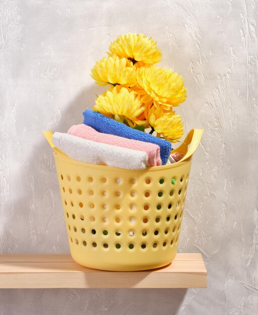 Eine Komposition aus Frühlingsfrische und Reinheit. Wäschekorb in gelber Farbe. Sauber gewaschene Handtücher in verschiedenen Farben. Schöne gelbe Blumen