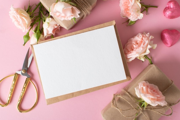 Eine Komposition zum Valentinstag aus ecopackaged Geschenken, einem Umschlag aus Kraftpapier und frischen Blumen auf einem hellrosa Hintergrund Vintage-Banner