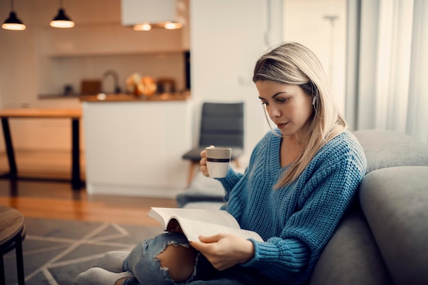 Eine konzentrierte Frau, die in ihrem gemütlichen Zuhause ein Buch liest und Kaffee trinkt