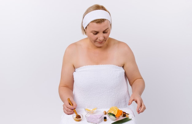Eine konzentrierte Frau mit einem Verband auf dem Kopf und einem Handtuch umwickelt macht aus natürlichen Produkten zu Hause eine Maske. Hochwertiges Foto