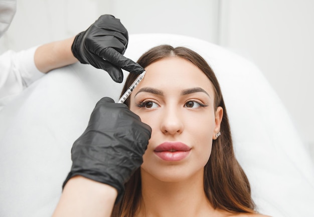 Eine Kosmetikerin macht Anti-Aging-Injektionen gegen Falten auf der Stirn im Gesicht einer schönen Frau Ästhetische Kosmetologie für Frauen in einem Schönheitssalon