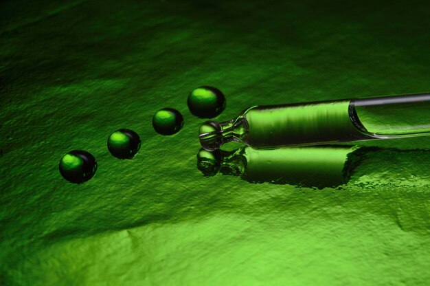 Eine Kosmetikpipette mit Flüssigkeit liegt auf einem grünen, mit Tropfen bedeckten Hintergrund. Nahaufnahme.