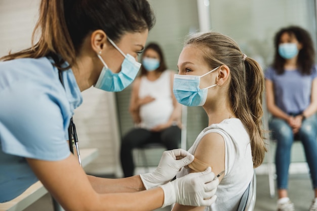 Eine Krankenschwester, die einem süßen Teenager-Mädchen ein Pflaster anbringt, nachdem sie den Covid-19-Impfstoff erhalten hat.