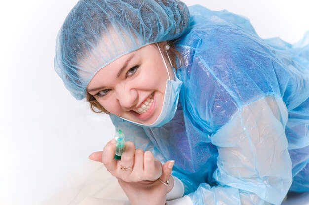 Eine Krankenschwester in Schlafrock und Maske mit einer Spritze in den Händen schaut in die Kamera und lächelt wütend