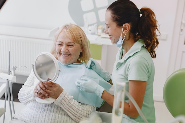 Eine Krankenschwester lächelt, während sie mit einem Patienten in der Hand auf einem Zahnarztstuhl sitzt.