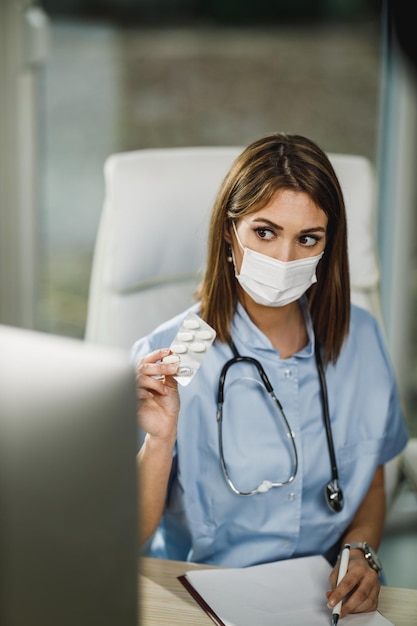 Eine Krankenschwester mit schützender Gesichtsmaske, die während der COVID-19-Pandemie einen Videoanruf mit dem Patienten am Computer führt.
