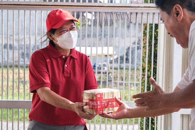 Eine Kurierin mit roter Mütze und Poloshirt überreichte einem Mann ein Paket