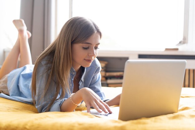 Eine lächelnde Frau, die sich vor ihrem Laptop auf das Bett legt Von zu Hause aus in Quarantäne arbeiten Soziale Distanzierung Selbstisolation