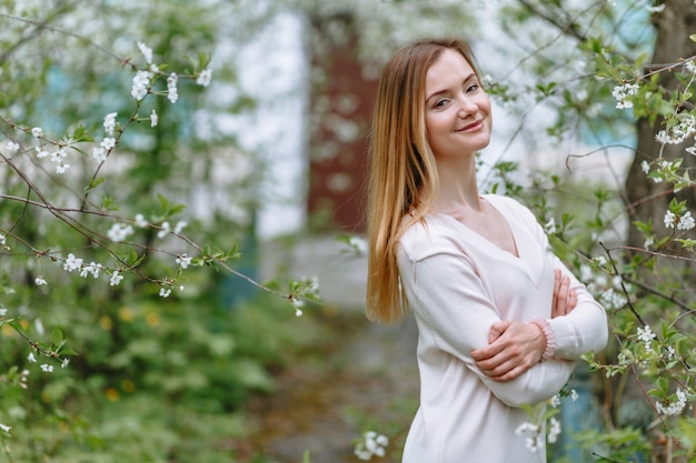 Eine lächelnde Frau in einer weißen Bluse steht in einer Kirschblüte