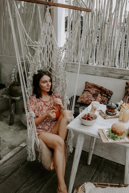 Foto eine lächelnde frau isst, während sie auf einer hängematte sitzt