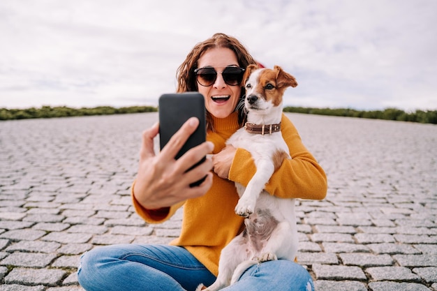 Eine lächelnde Frau macht ein Selfie, während sie mit einem Hund im Freien sitzt