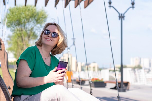 Eine lächelnde Frau mit Sonnenbrille, die mit Freunden telefoniert und sich im Sommer im Park verabredet