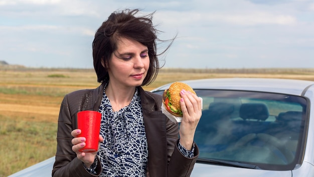 Eine lächelnde Frau vor blauem Himmel isst gerade einen Hamburger.