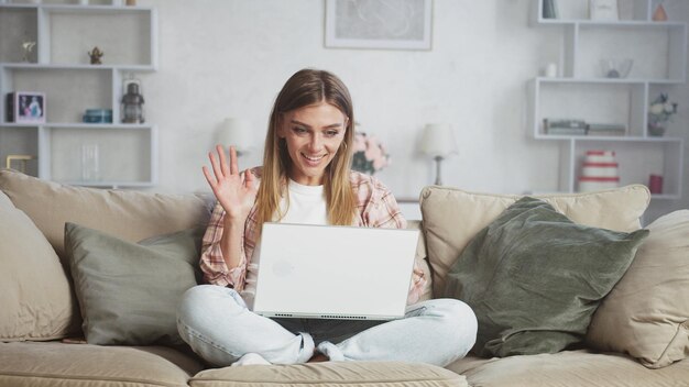 Eine lächelnde Frau winkt beim Laptop während eines Videogesprächs zu Hause