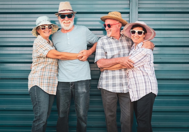 Eine lächelnde gruppe von vier älteren menschen in freundschaft umarmt sich an einer blauen wand männer mit bart alle menschen mit hut fröhliche und entspannte gesichter für rentner