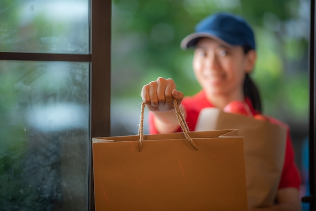 Eine lächelnde junge asiatische Frau liefert Waren vor der Haustür, Online-Einzelhandelskonzept, schnelle Lieferung, urbanes Lifestyle-Konzept, Online-Shopping-Service, Transport.
