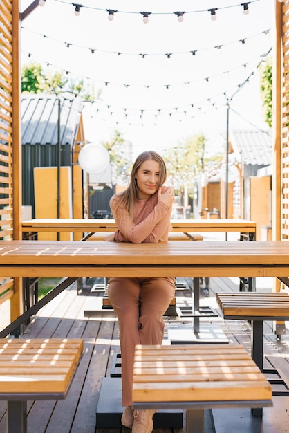 Eine lächelnde junge attraktive Frau sitzt an einem Tisch eines Cafés im Freien auf einer Sommerterrasse