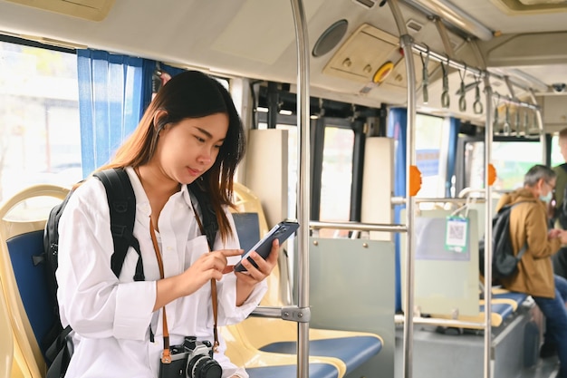 Eine lächelnde junge Frau benutzt beim Busreisen ein Mobiltelefon. Öffentliches Verkehrskonzept