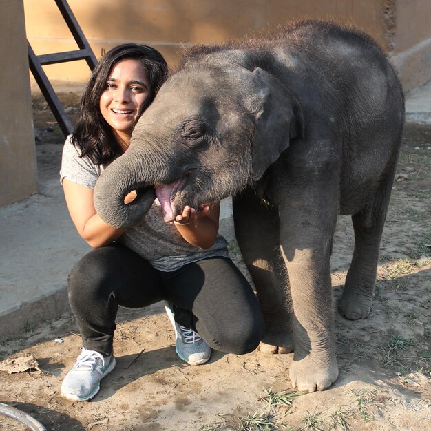 Eine lächelnde junge Frau mit einem Elefantenkalb im Zoo in voller Länge