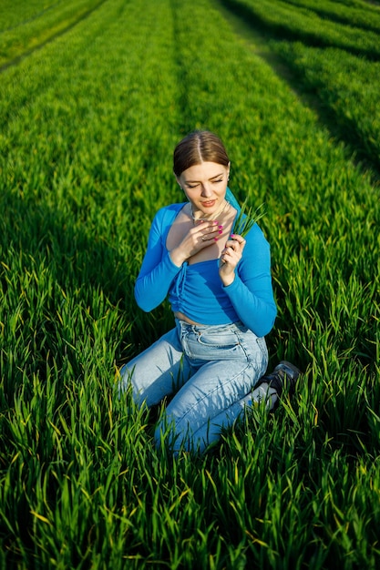 Eine lächelnde junge Frau sitzt auf einem weitläufigen Feld im grünen Gras