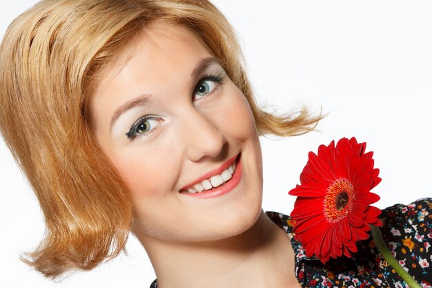 Eine lächelnde schöne junge Frau in einem weißen Kleid mit einer hellen roten Blume nahe ihrem Gesicht