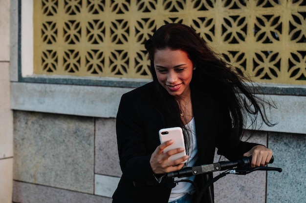 Eine lateinamerikanische Frau mit Bart und einem Roller, die auf sein Handy schaut