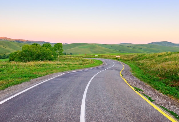 Eine leere Autobahn zwischen grünen Hügeln im Morgengrauen unter blauem Himmel Sibirien Russland