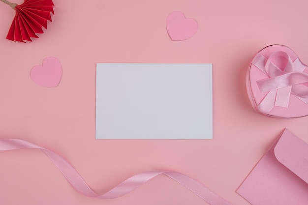 Eine leere Karte, umgeben von rosa Herzen, ein Band, ein Geschenk und ein Umschlag Einladungsmodell