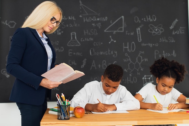 Eine Lehrerin unterrichtet Schulkinder, die an einem Schreibtisch sitzen und Probleme lösen. Internationales Team Zurück zur Schule