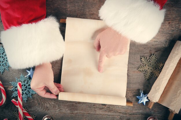 Eine Liste von Weihnachtswünschen in Santa Claus Händen auf Holztisch on