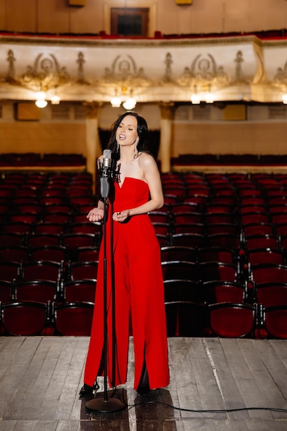 Eine luxuriöse Schauspielerin in einem roten Kleid singt mit einem Mikrofon in den Händen auf der Bühne