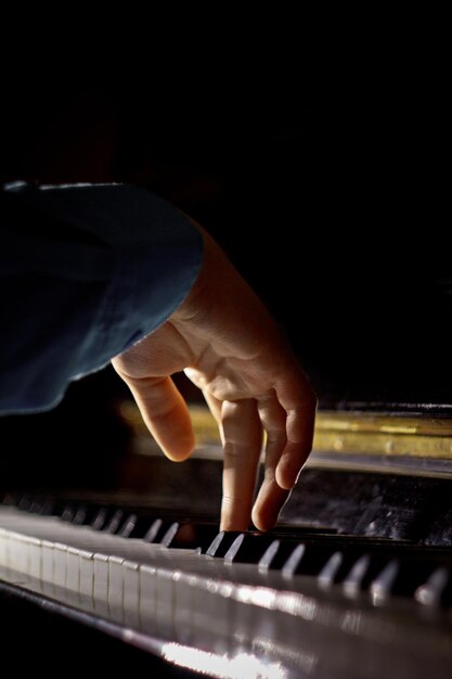 Foto eine männliche hand auf dem klavier die handfläche liegt auf den tasten und spielt das tastaturinstrument in der musikschule schüler lernt mit den händen zu spielen pianist schwarz dunkler hintergrund vertikal