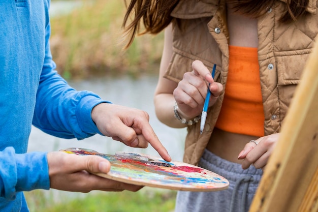 Eine männliche Hand, die Farben hält, und eine Frau hält Pinsel