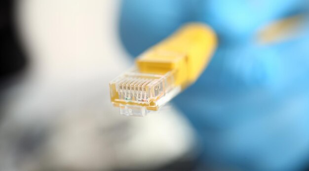 Eine männliche Hand in blauen Schutzhandschuhen hält einen Netzwerkstecker. Der LAN-Konstrukteur dekonstruiert die Verbindung von Clients zum Internet auf Basis von XPON und ADSL