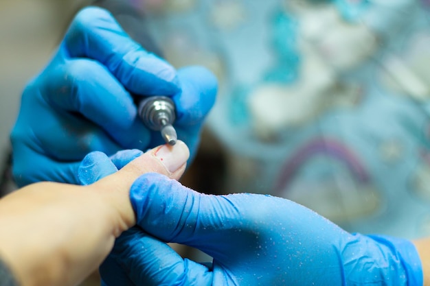 Eine Maniküre in blauen Handschuhen macht eine Maniküre mit einem Gerät. Nagelhautbehandlung