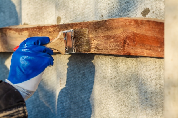 Eine Mannhand mit dem blauen Handschuh, der Pinsel hält, der Holzlack aufträgt