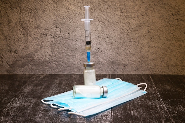 Eine medizinische Glasflaschenampulle und eine medizinische Einwegspritze mit einer Nadel. Das medizinische Konzept zeigt ein medizinisches Reagenzglas und Impfstoffe gegen das Virus. dunkler Holztisch