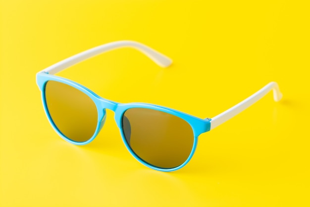 Eine minimalistische Anordnung der blauen Sonnenbrille auf einem hellen gelben Hintergrund