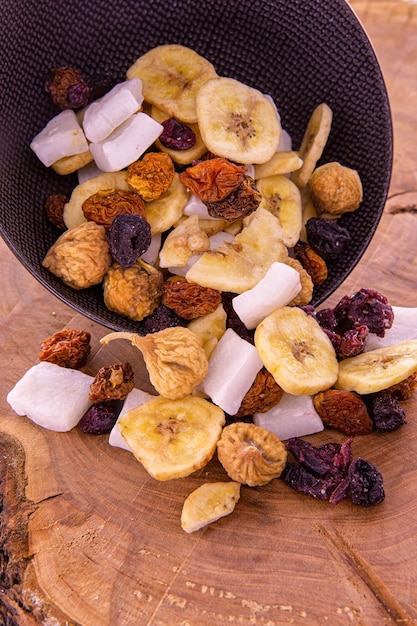 eine Mischung aus geschnittenen getrockneten Früchten und Beeren, Nüssen, die aus einer dunklen Tasse auf einem Holz verschüttet wurden