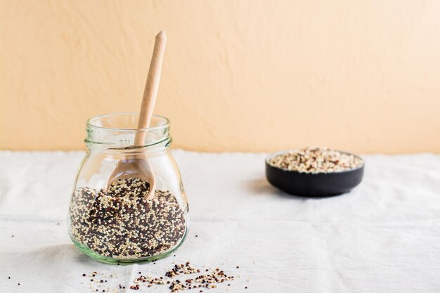 Eine Mischung aus rohem, weißem, rotem und schwarzem Quinoa und einem Holzlöffel in einem Glas auf einem Tuch Gesundes glutenfreies Essen