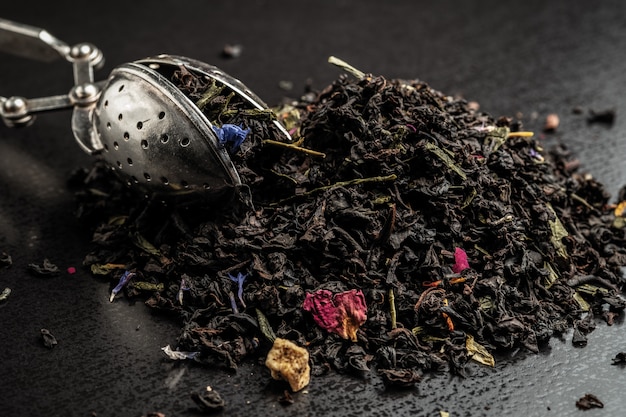 Eine Mischung von trockenen Blättern des schwarzen und grünen Tees mit Blumen auf einem dunklen Hintergrund, Teesieb