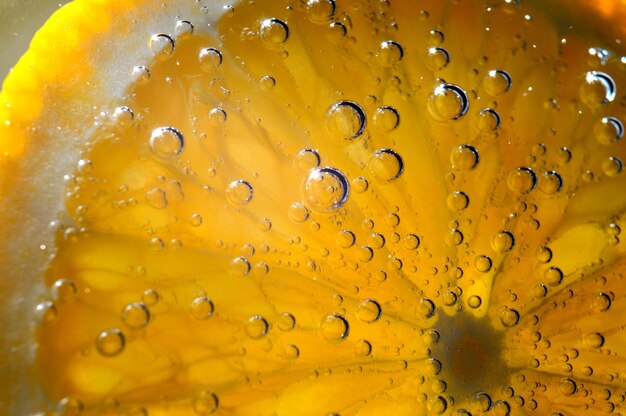 eine mit Blasen bedeckte Orangenscheibe liegt in einem Glas mit Sprudelwasser. Nahaufnahme.