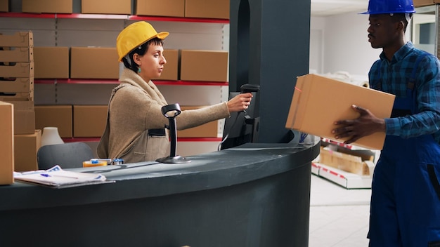 Eine Mitarbeiterin führt eine Bestandsinventur mit einem Scanner durch und scannt Barcodes auf Kartons mit Waren. Frau im Overall plant den Versand von Bestellungen, Industrieprodukte im Lagerraum.