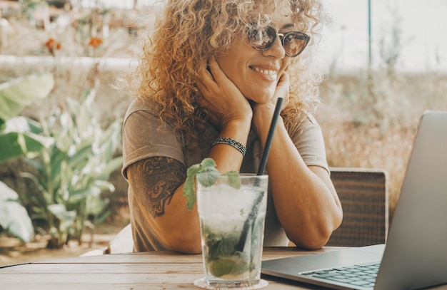 Eine moderne digitale Arbeiterin genießt die Zeit, im Sommer mit Cocktail-Mohito im Café zu sitzen und an Laptop und Online-Internetverbindung zu arbeiten Digitale Nomaden-Lifestyle-Frauen lächeln glücklich