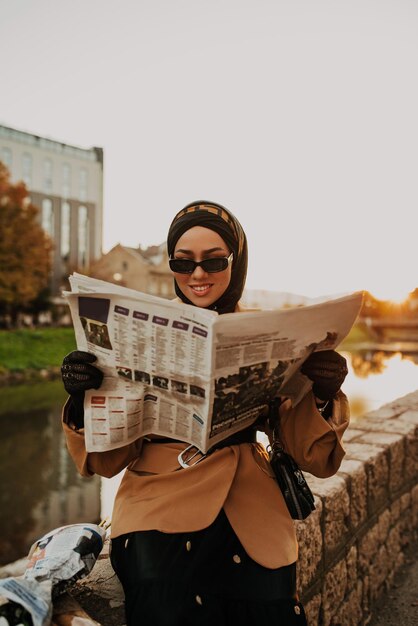 Eine moderne muslimische Frau mit Kopftuch geht durch die Stadt, während sie eine Zeitung und Brot in der Hand trägt.