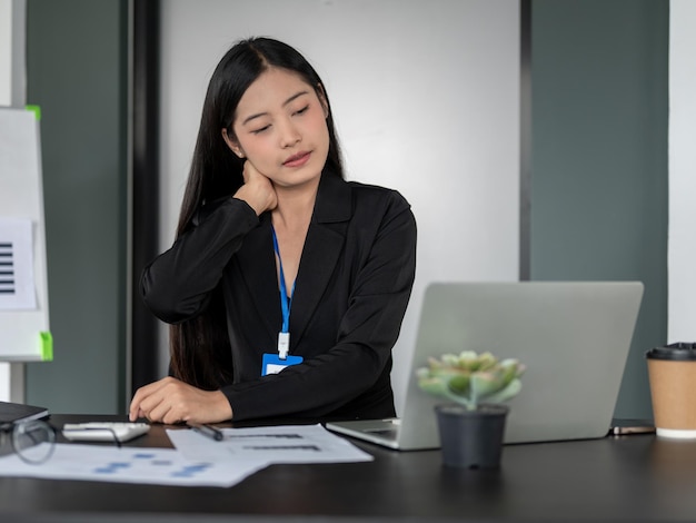 Eine müde asiatische Geschäftsfrau, die unter Nackenschmerzen leidet, weil sie überarbeitet ist