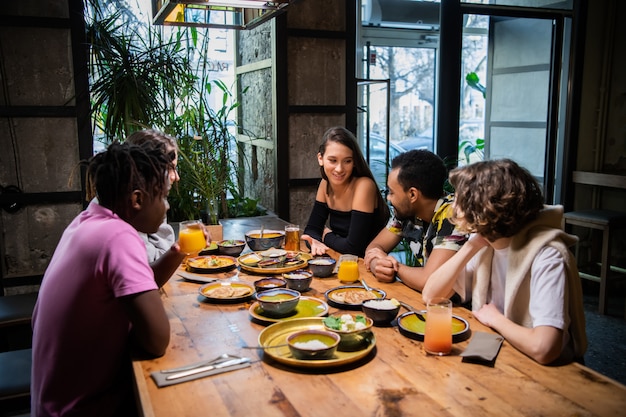 Eine multikulturelle Gruppe junger Leute in einem Café, die asiatisches Essen essen, Cocktails trinken, sich unterhalten