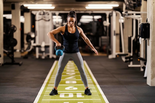 Eine muskulöse Sportlerin hebt Kettlebells und macht Bizepsübungen im Fitnessstudio